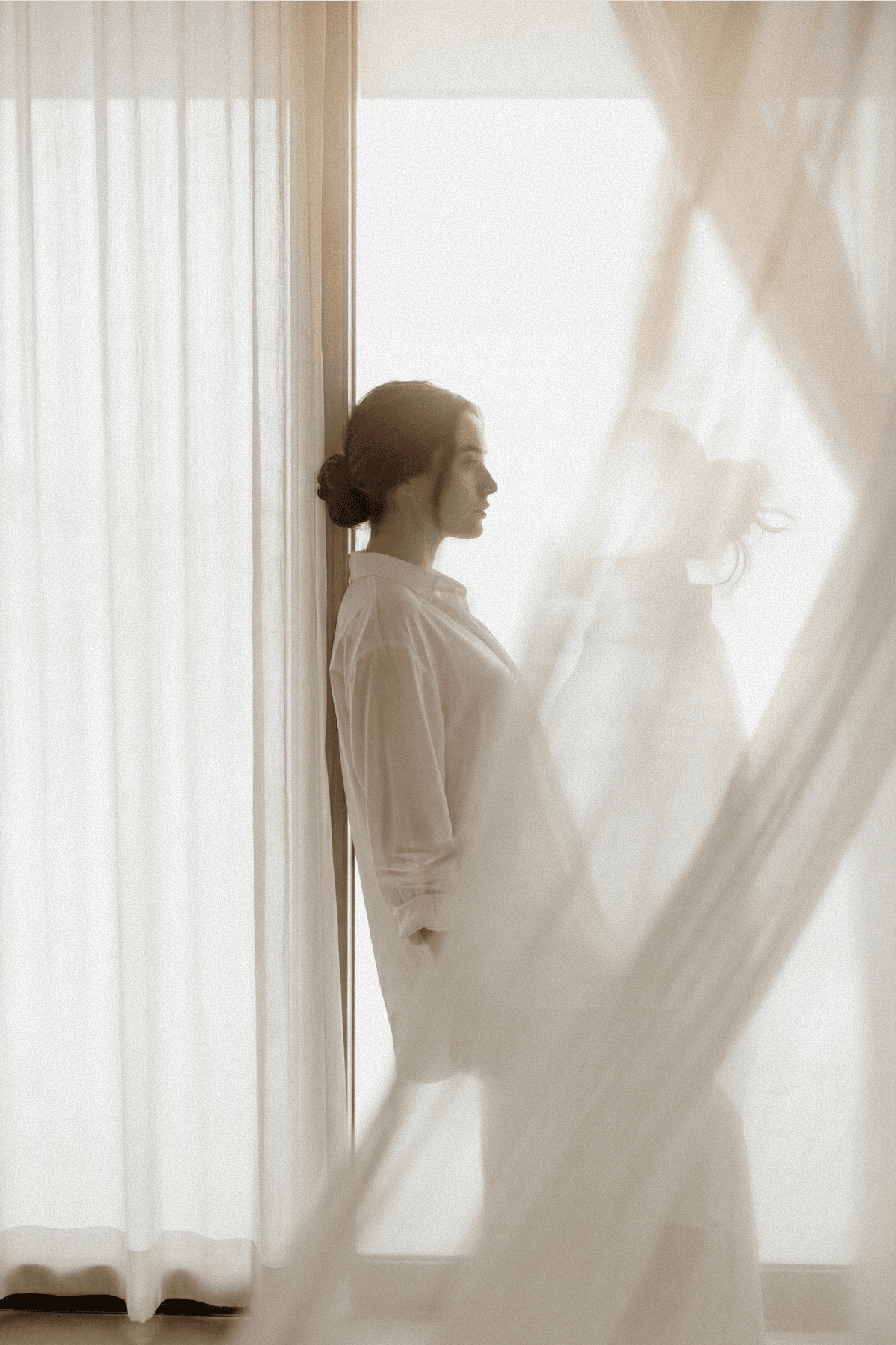 Woman standing beside sheer curtains